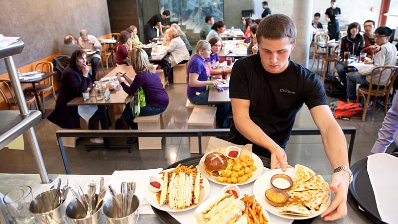 Cultivate employee grabbing a plate of food while students sit at tables.