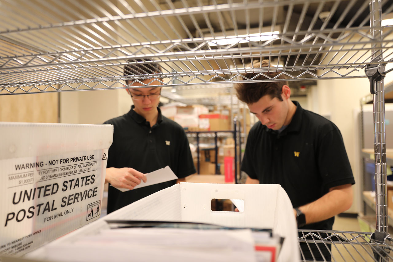 Two students in matching black shirts sorting mail