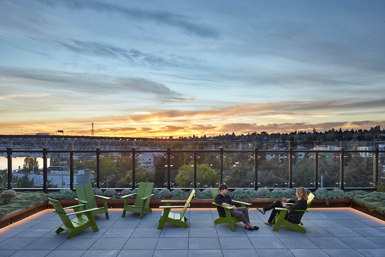 A sunset view from a rooftop deck with green chairs.