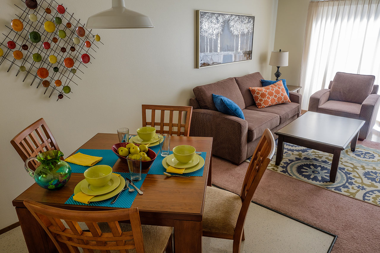 A living room in Blakeley Village with a set table, couches, chairs, and coffee table.