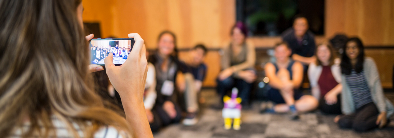 A student takes a picture of a group of students sitting and smiling.
