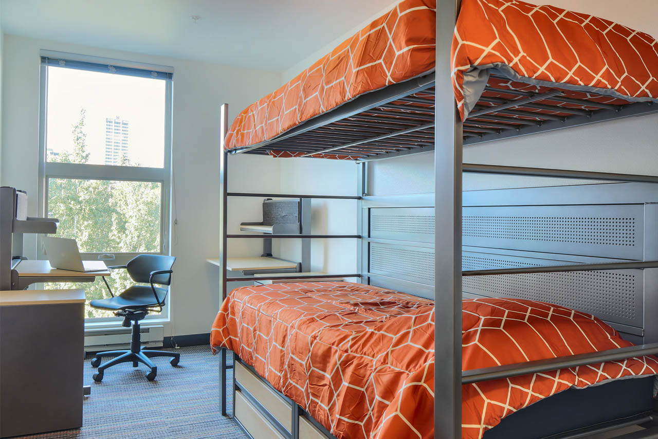 A double room Mercer Court with a bunk bed with orange sheets and a desk.