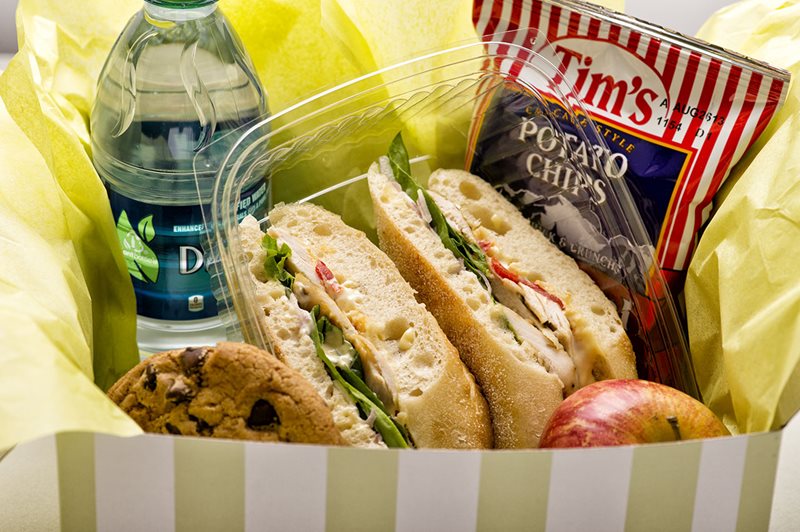 A box with a sandwich, cookie, chips, water, and apple.