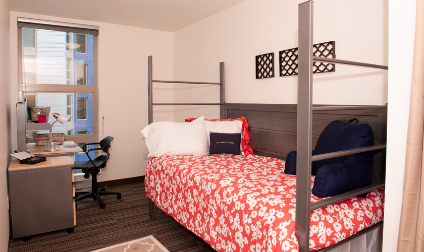A single room in Mercer Court with a twin bed with red sheets.