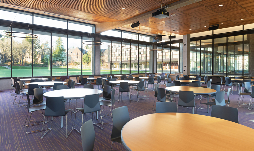A large room with round tables and chairs next to Denny Field.