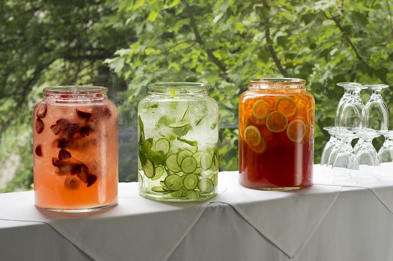 Three glass containers with fruit juice next to stacked glasses.