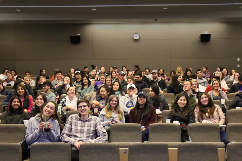 A group of students sit in a lecture hall smiling.
