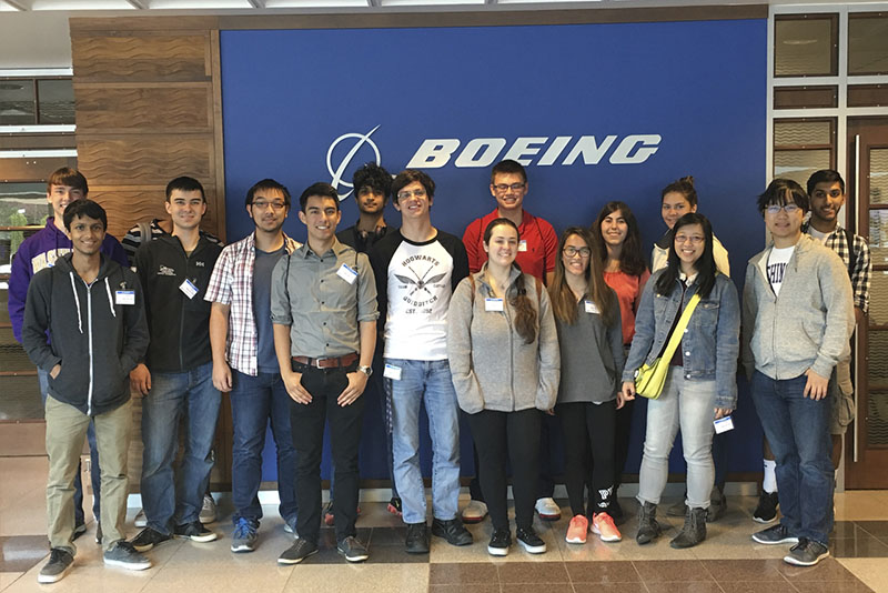 A group of students smiling in front of a Boeing sign.