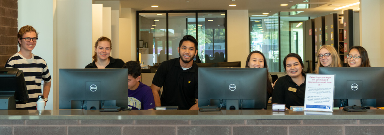 A group of student employees smile behind computers at Willow Desk.