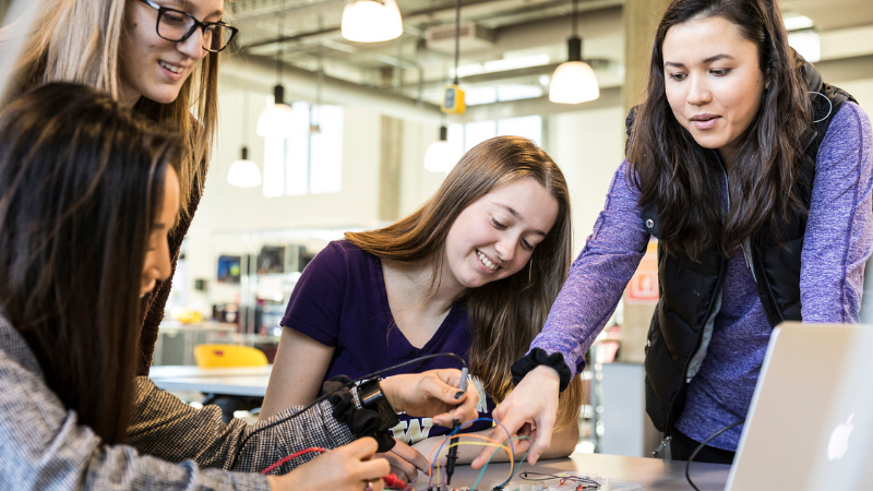 Group of four women working on a device with wires for their bio engineering capstone project.
