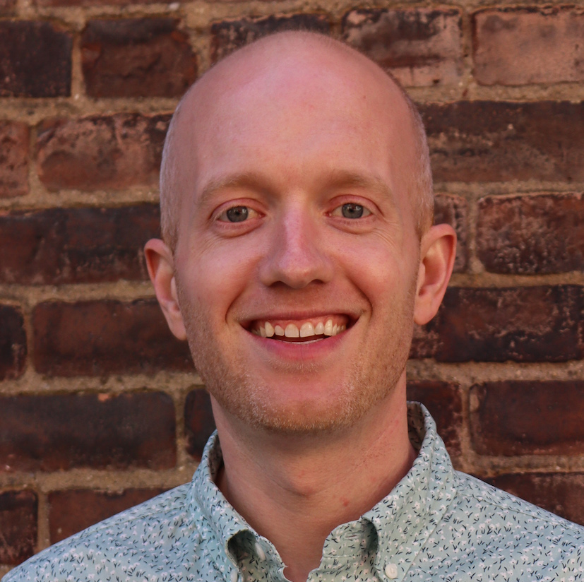 Kevin Conn smiling in front of a brick wall.