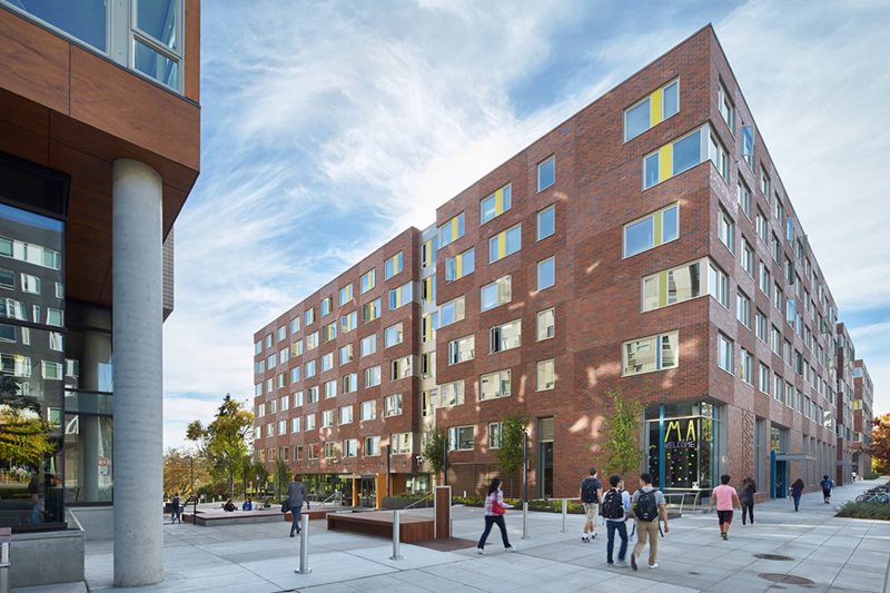 A group of students walking next to a brown building.