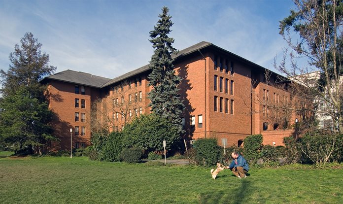 A person playing with a dog in the grass outside a brick building.