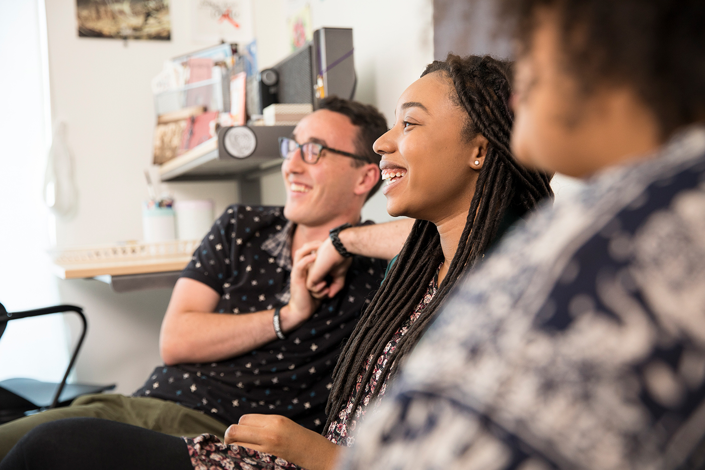 Three students smiling in a dorm room.