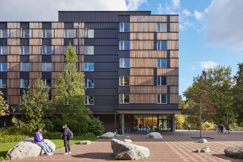 A black and brown building with trees and rocks in front of it.