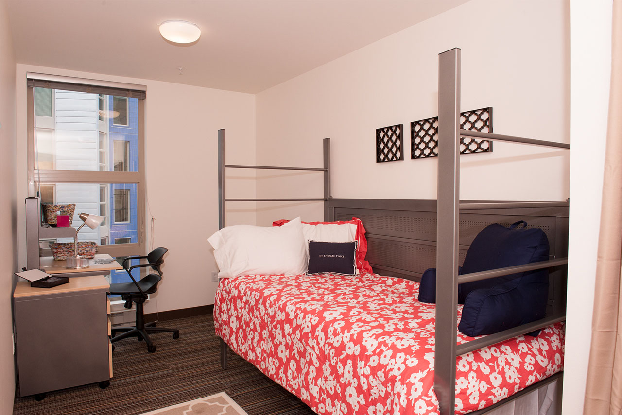 Room with twin bed with red sheets and desk.