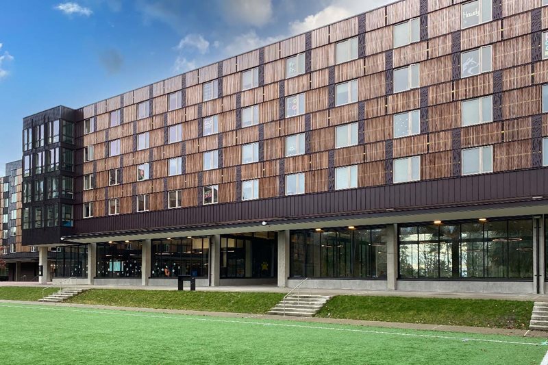 A black and brown building with a green outdoor field.