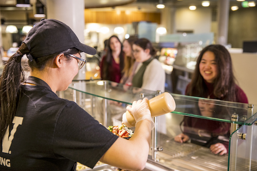 Dining employee pours sauce on students meal