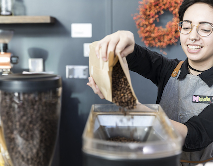 A barista pours coffee beans into a coffee machine