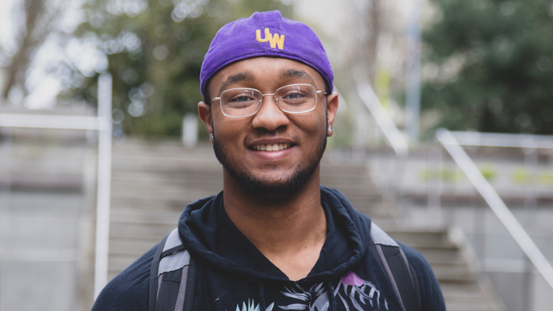 A student with glasses and a purple hat smiling.