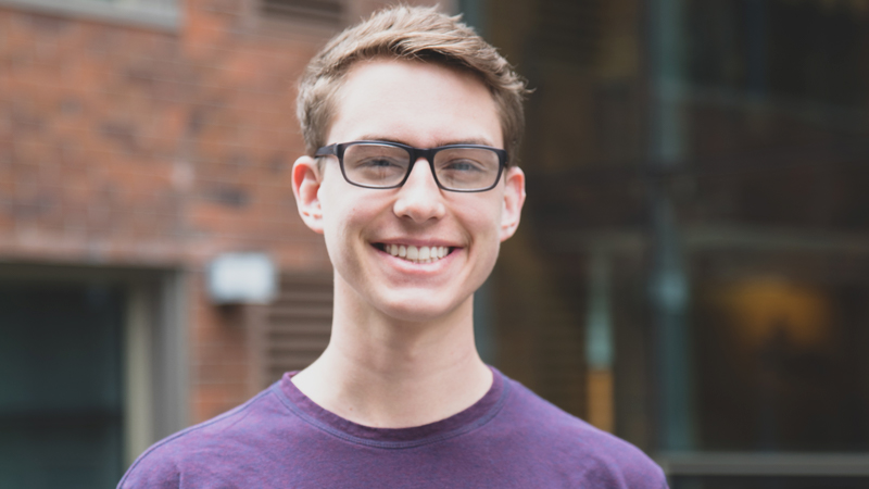 A student with glasses and a purple shirt smiling.