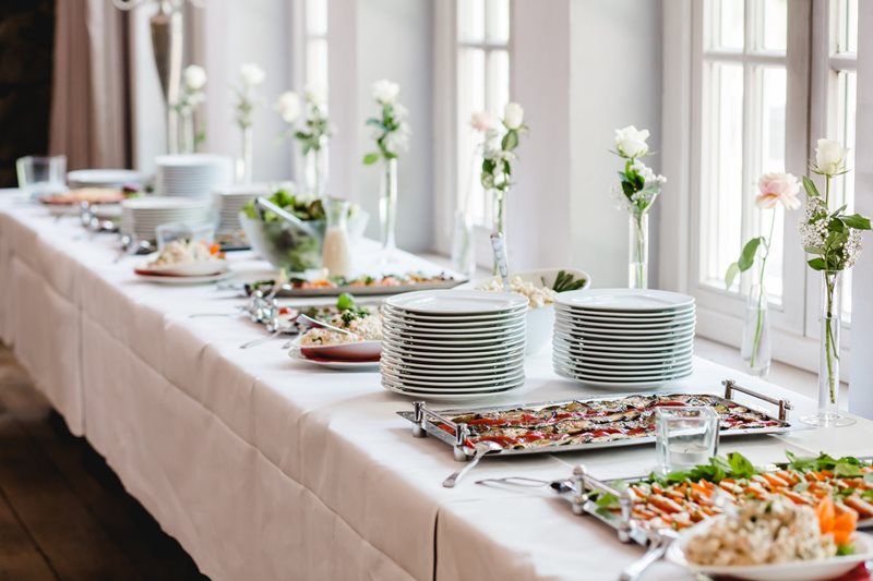 Buffet table with food, plates, and flowers at a wedding reception.