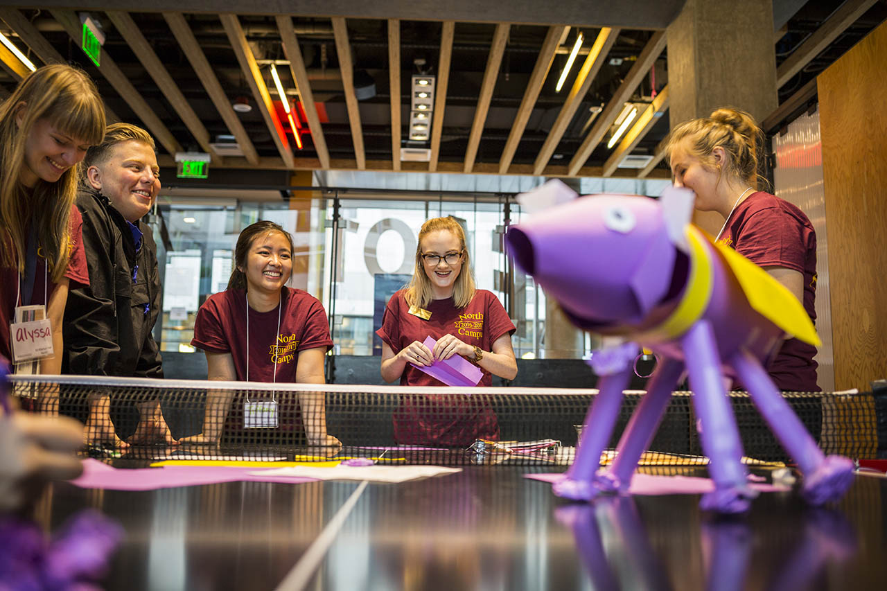 Five students smiling around a ping pong table in Area 01.