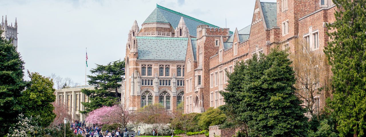 Students walking next to a brick building with a green roof and trees.