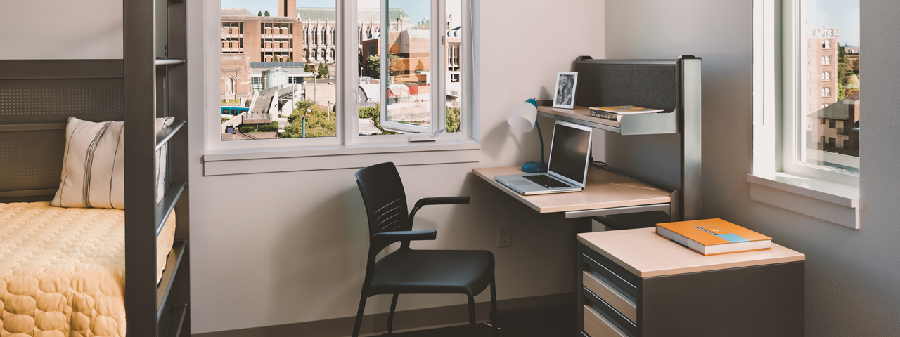 A dorm room with a twin bed, desk, and dresser.