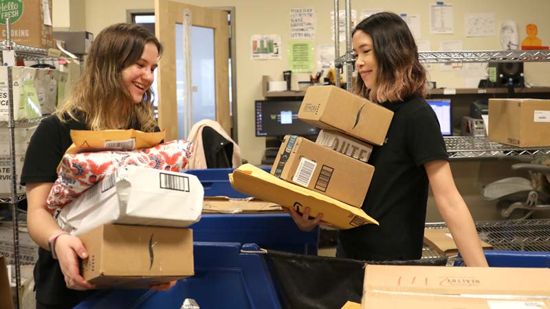 Students carrying packages in the mail room.