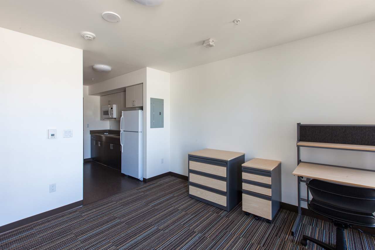 A dorm room in Mercer Court with a desk, drawers, and a kitchen.