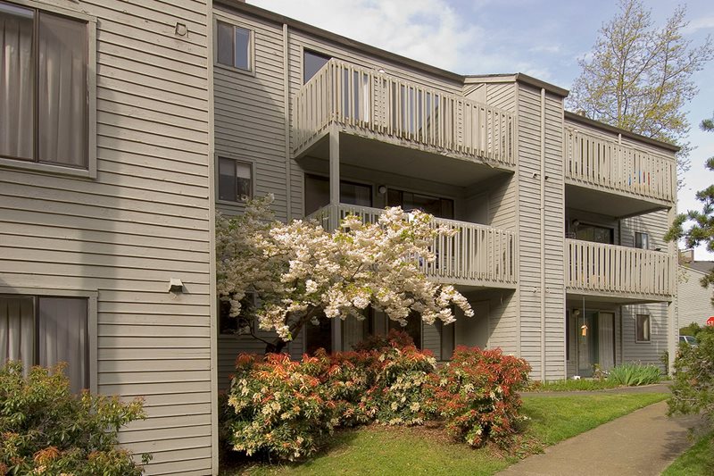 A brown building with trees and flowers in front of it.