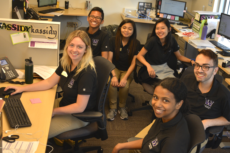 A group of student employees sitting in cubicles smile.