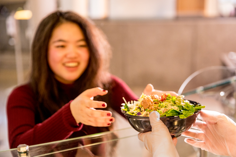 Employee handing salad bowl to student