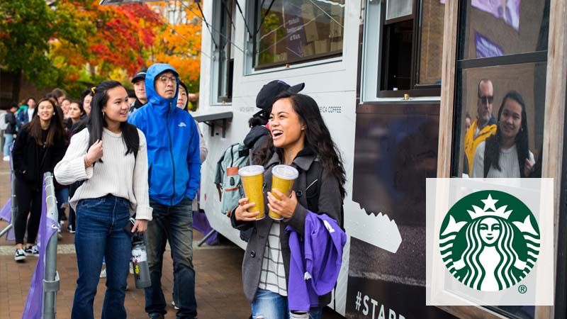 A student carrying two cups while a group of people wait in line to order at Starbucks Food Truck.