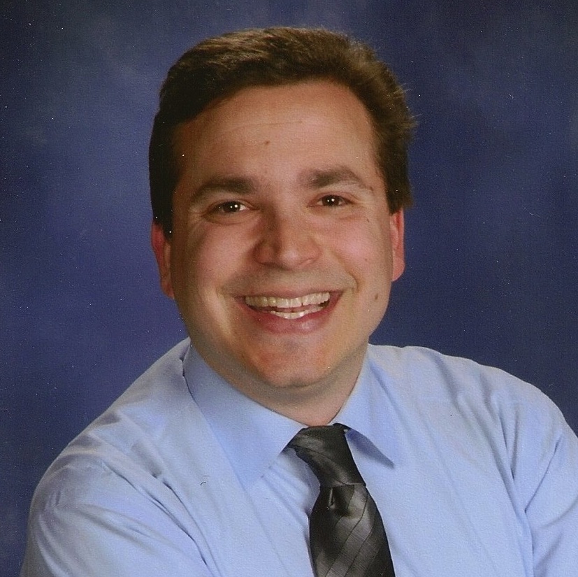 Cory Shapiro smiling in front of blue background.