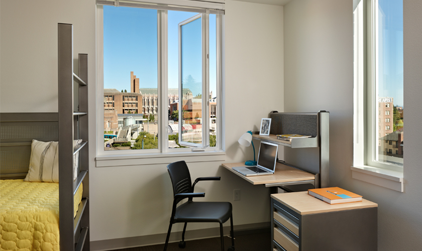 A dorm room with a twin bed, desk, and dresser.