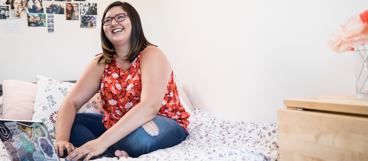 A student sitting on a bed smiling.