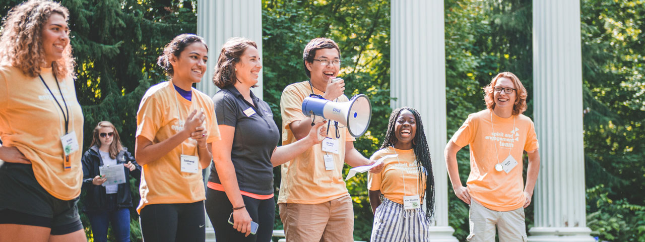 A group of students in orange shirts speaking to a crowd at RA training.