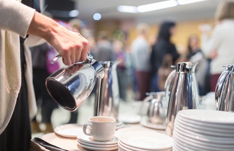 A person pouring milk from a silver jug into a mug.