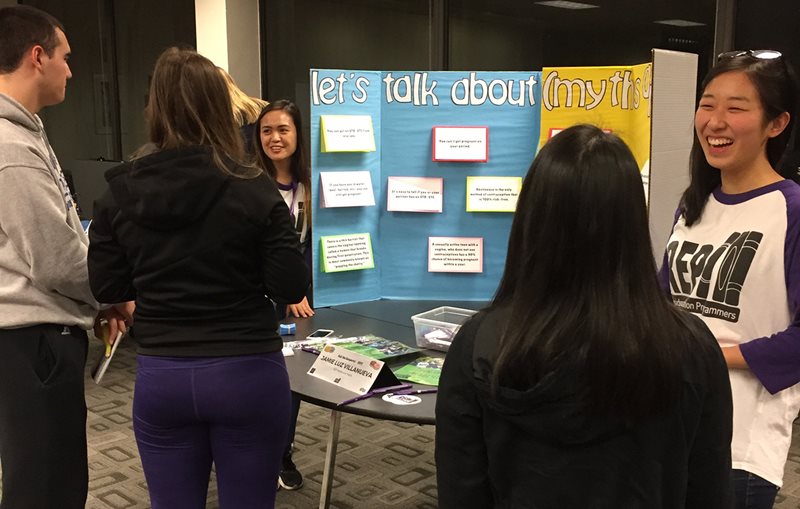 Students presenting a trifold poster to other students.