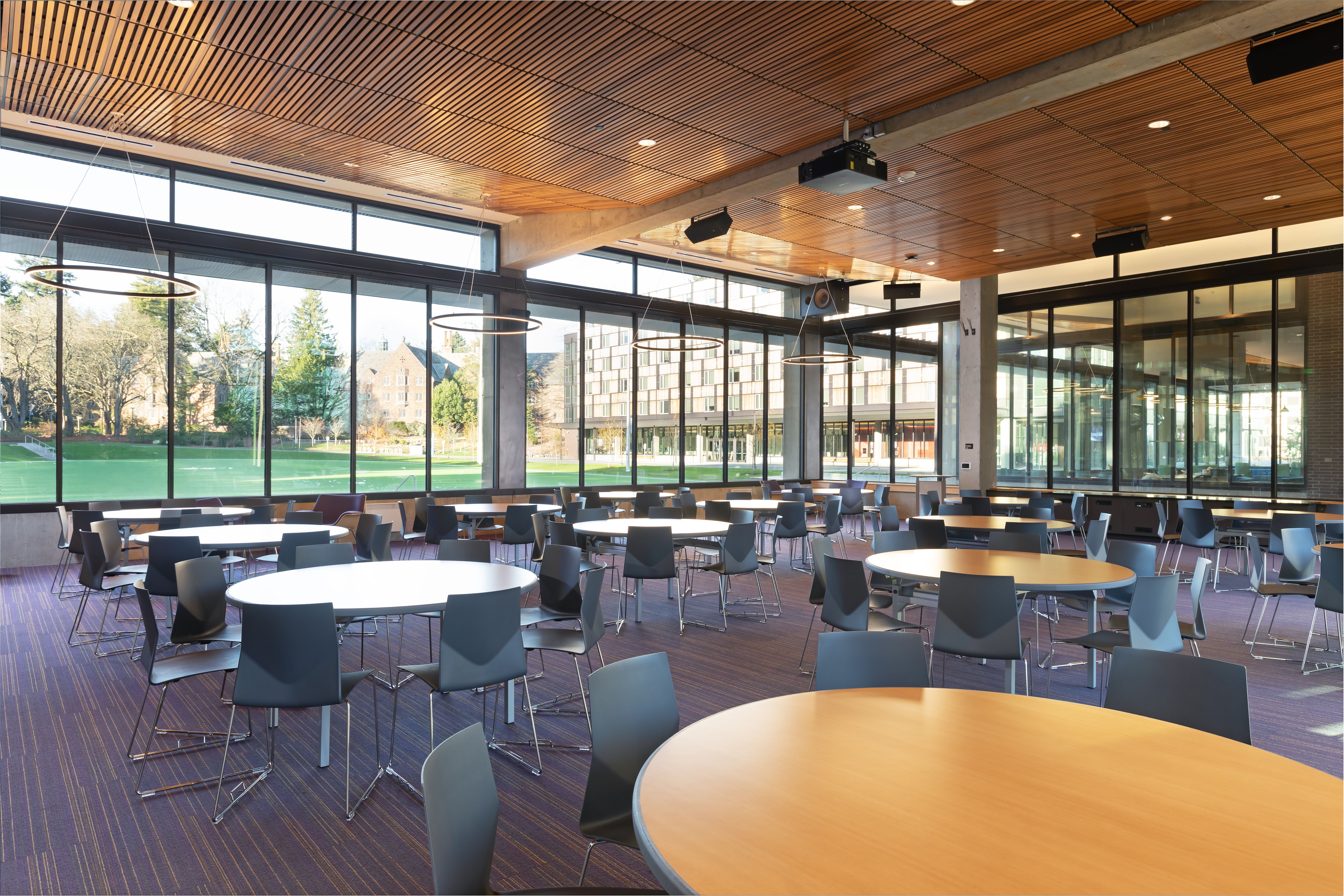 Large room with circle tables and windows looking at turf field.