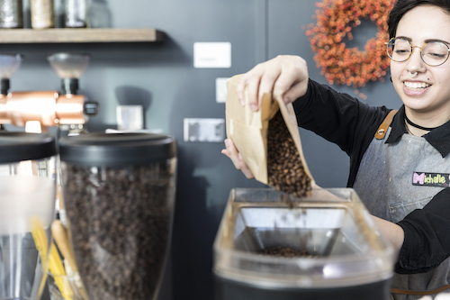 A barista pouring coffee beans into a coffee machine.